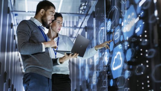 Male IT Specialist Holds Laptop and Discusses Work with Female Server Technician. They’re Standing in Data Center, Rack Server Cabinet with Cloud Server Icon and Visualization. Male IT Specialist Holds Laptop and Discusses Work with Female Server Technician. They're Standing in Data Center, Rack Server Cabinet with Cloud Server Icon and Visualization.
